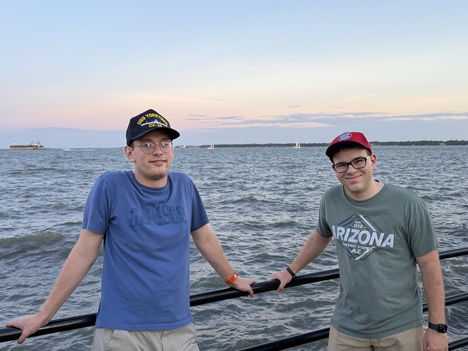 The boys on the seawall, harbor behind, hats on.