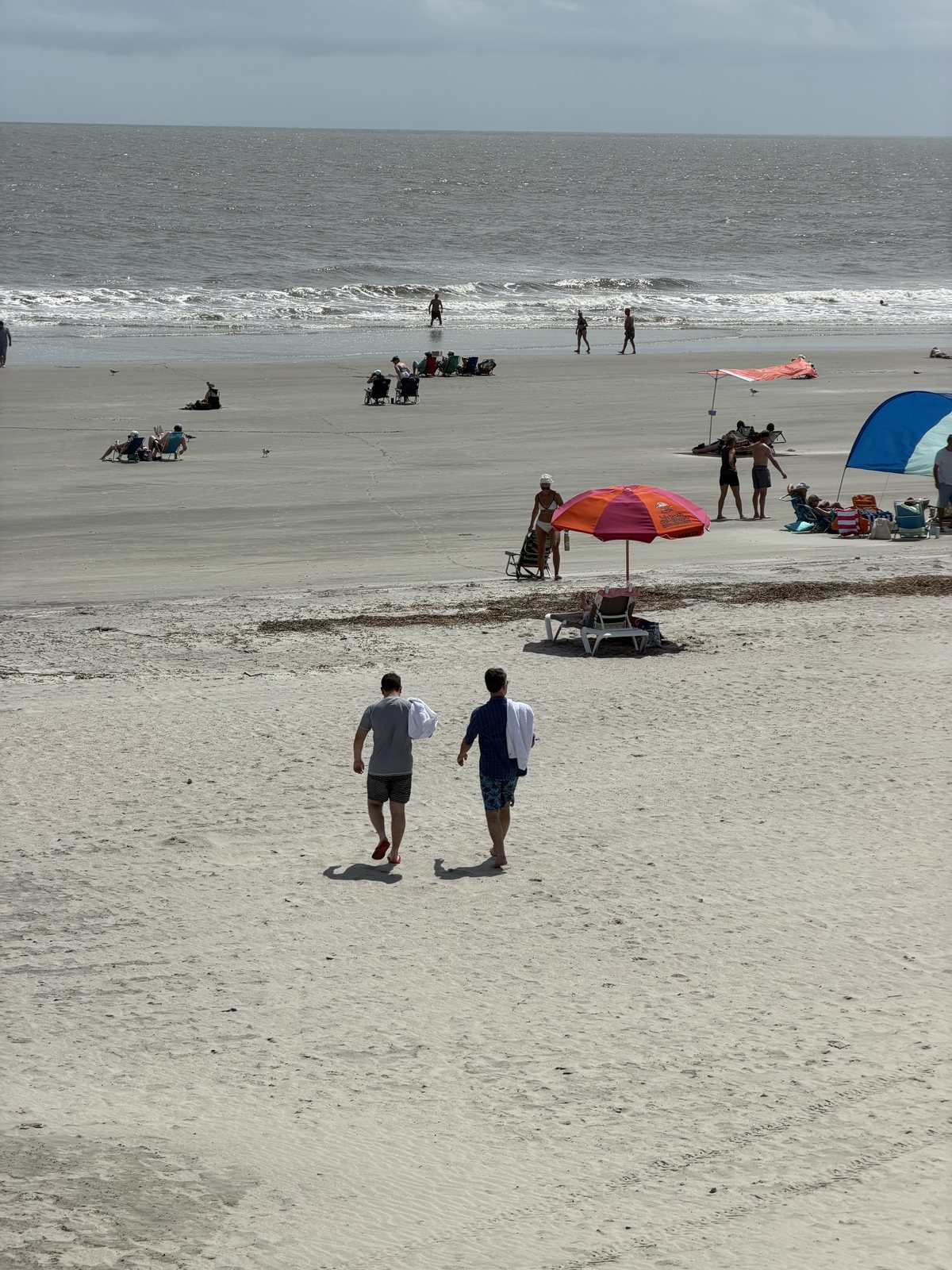 The beach from the pier. Umbrellas, walkers, and two of ours heading for the water.